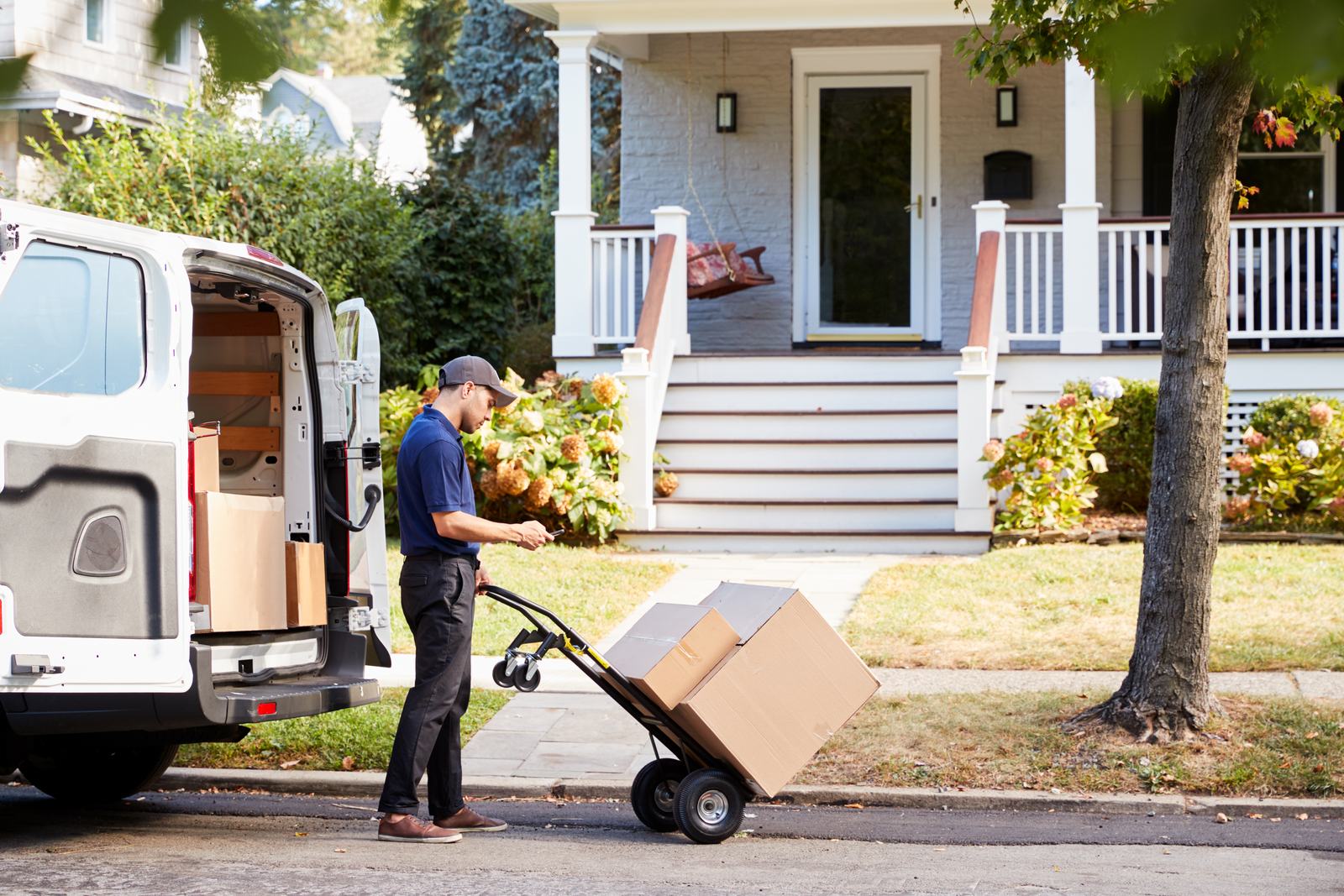 A courier wheeling boxes to a house