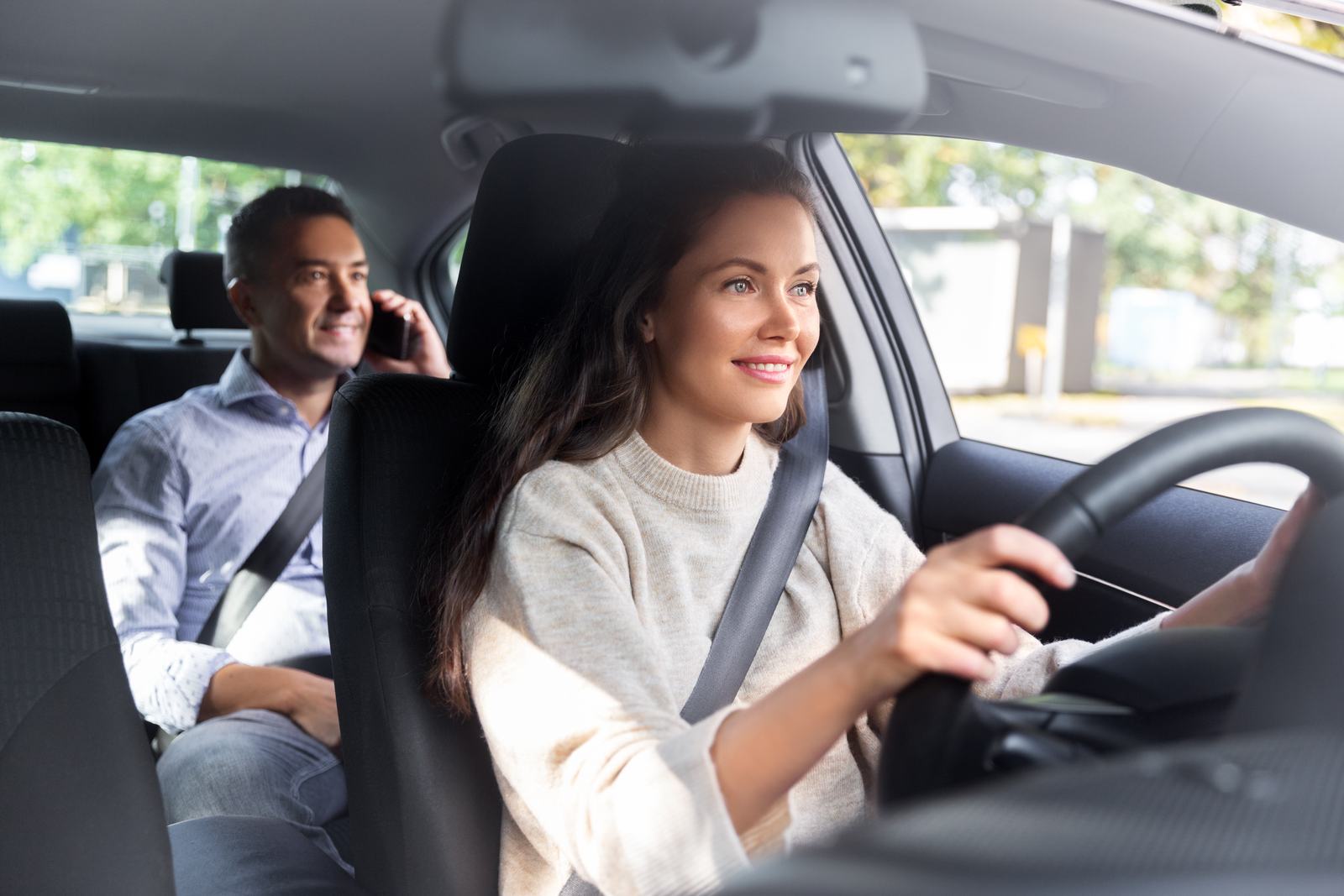 A driver smiling with a passenger in the back seat